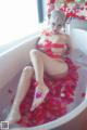 A woman in a bathtub with rose petals on the floor.