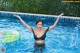 A woman in a black bikini standing in a pool with her arms outstretched.