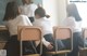 A group of girls sitting at desks in front of a blackboard.